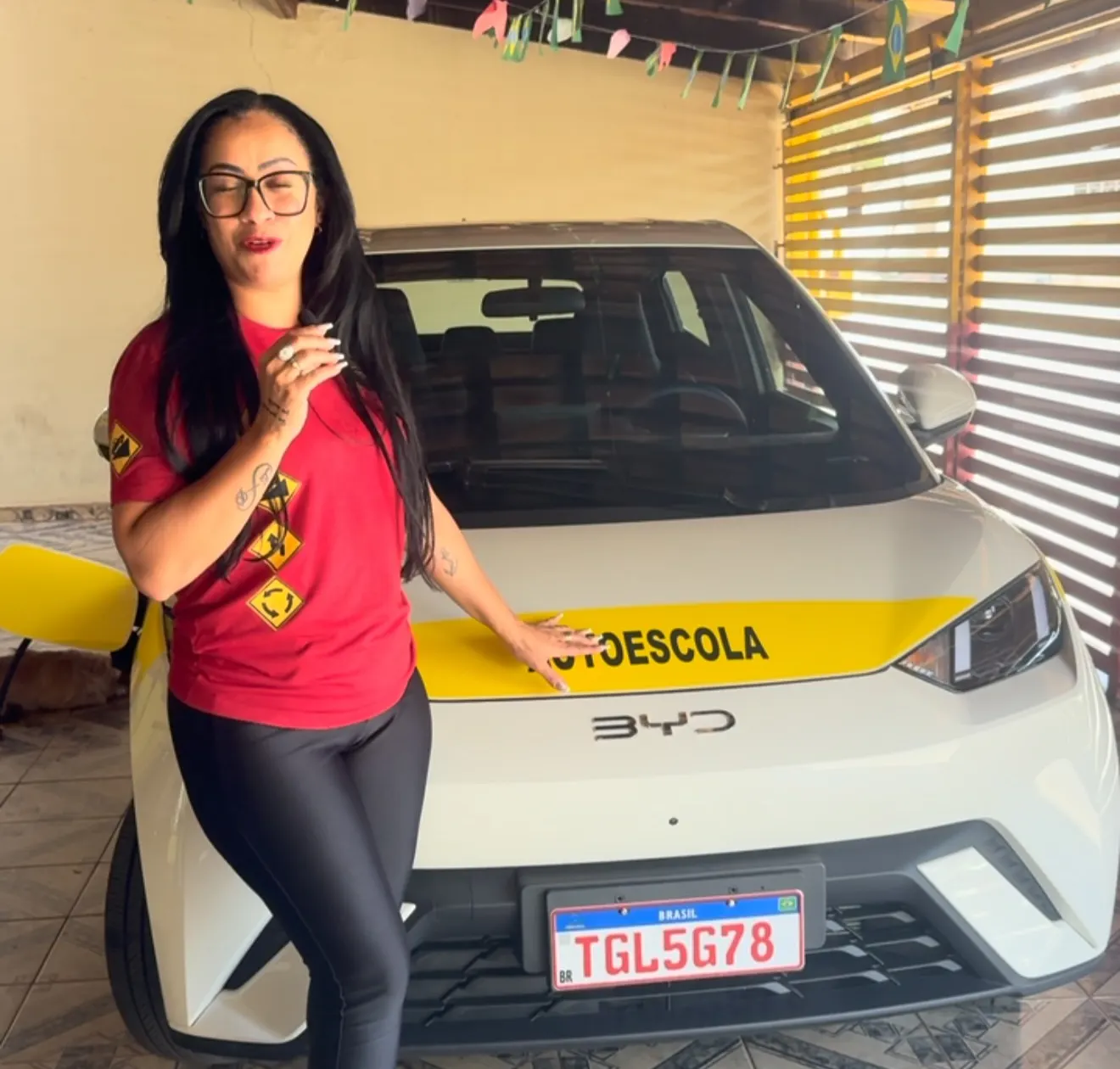 Tia Tati, instrutora da Jacarandá, ao lado do carro elétrico BYD de aulas